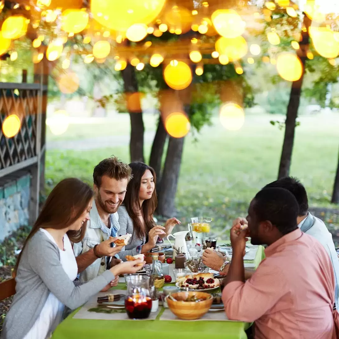 A group of people eating a meal at a table under a tree