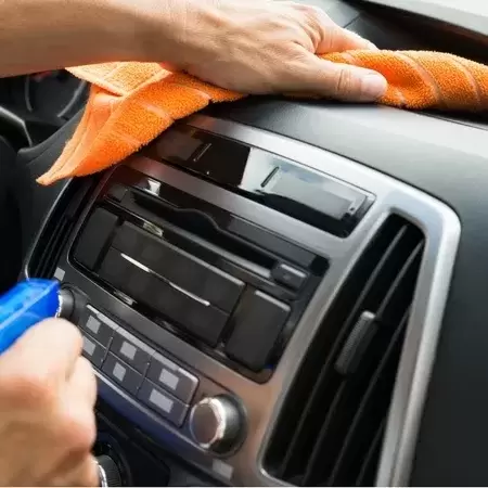 Close up of hands cleaning the interior of a car with a spray bottle of cleaner and a microfiber cleaning cloth