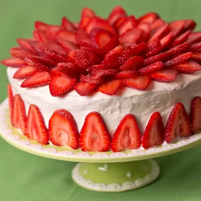 Strawberry garnished cake on a pedestal atop a spring-green tablecloth.