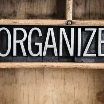 Pictured: A wooden shelving unit with a black-and-white sign with the word Organize in block letters on it. 