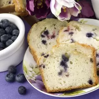 PIcture: a small bowl of fresh blueberries next to a loaf of blueberry infused sweet bread.