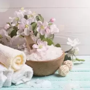 three towels rolled up and sitting next to a bowl of bath salts with lilies on top