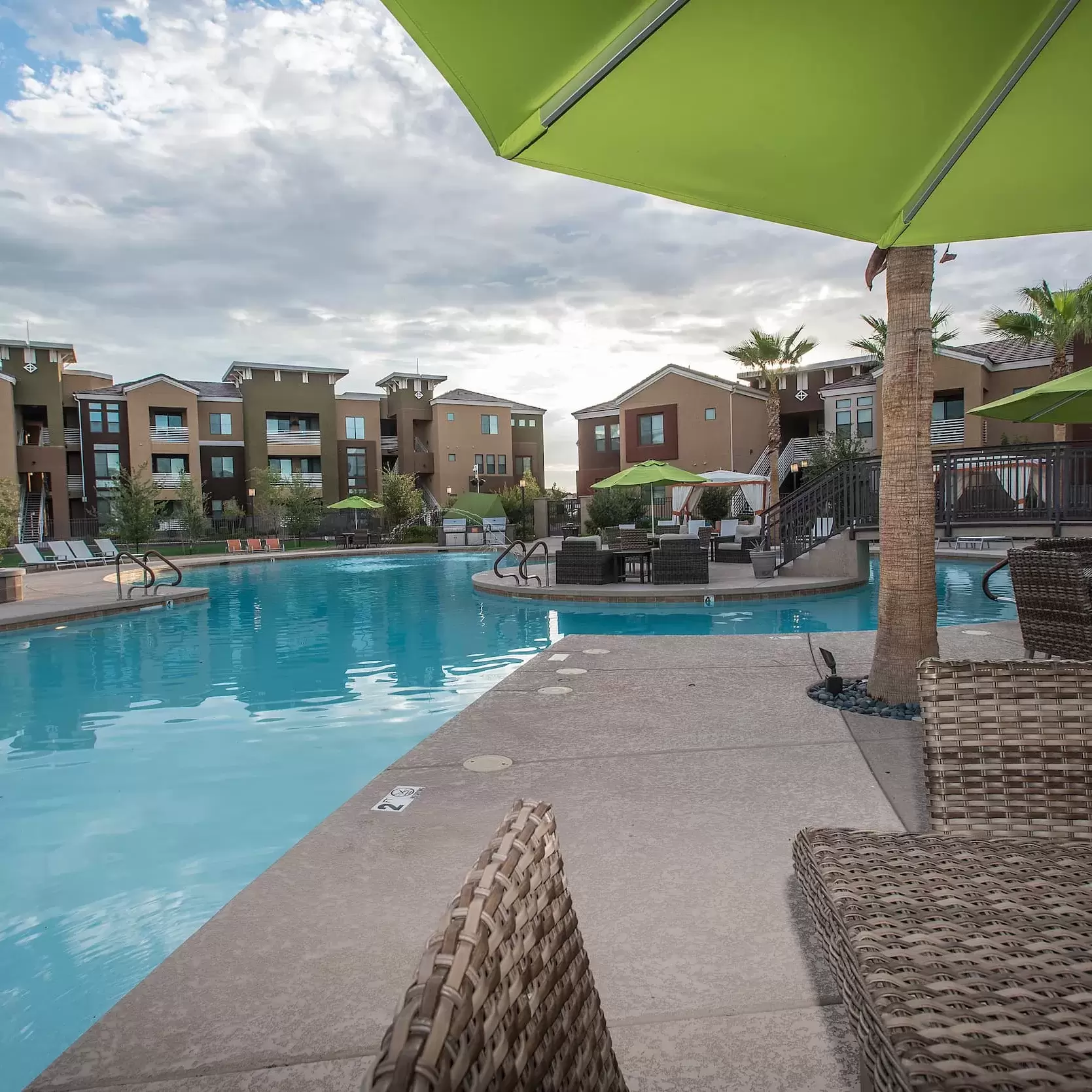 Chairs and tables with umbrellas on the pool deck at the luxury apartment complex.