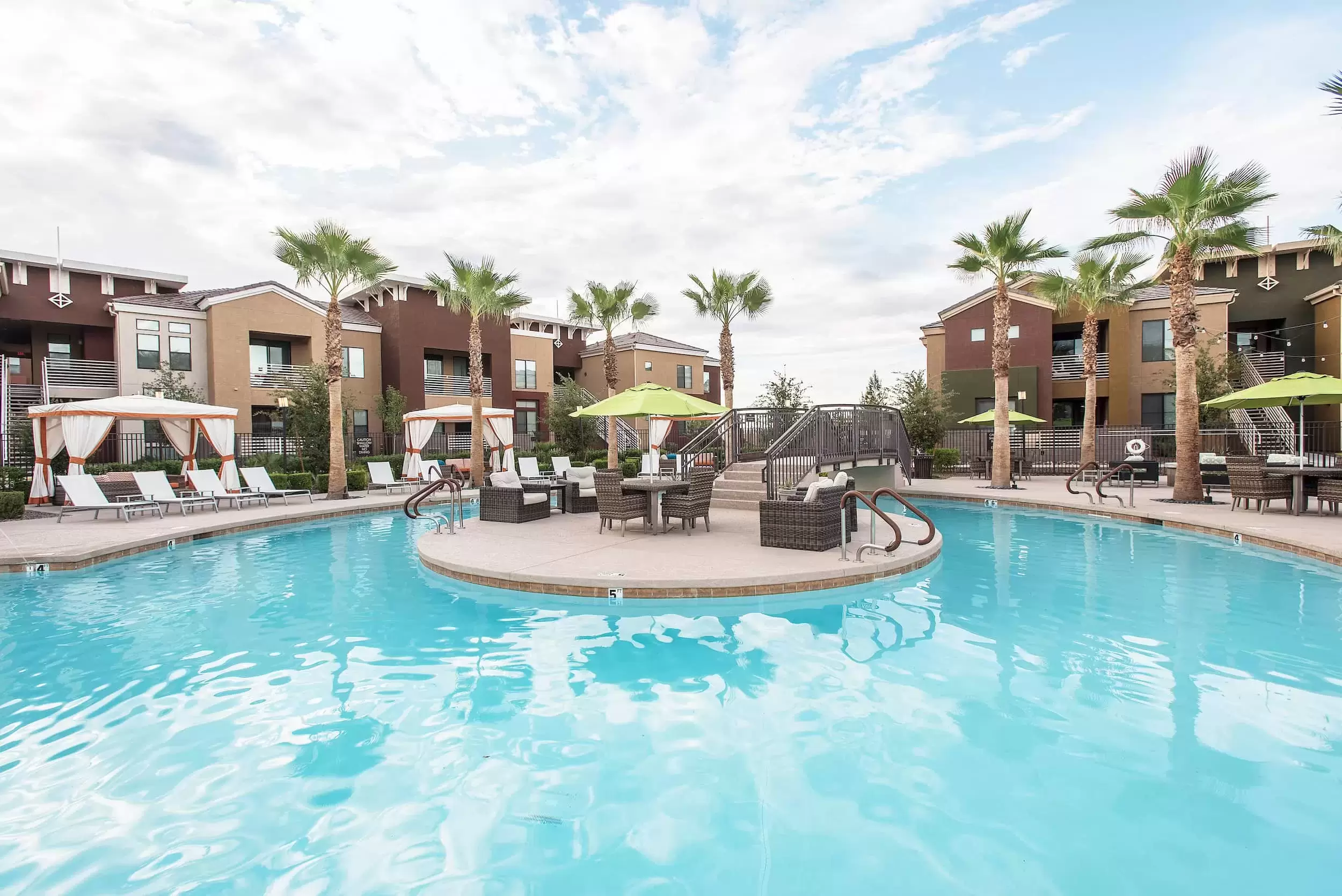 A view of the pool and patio, surrounded by palm trees and apartment buildings.