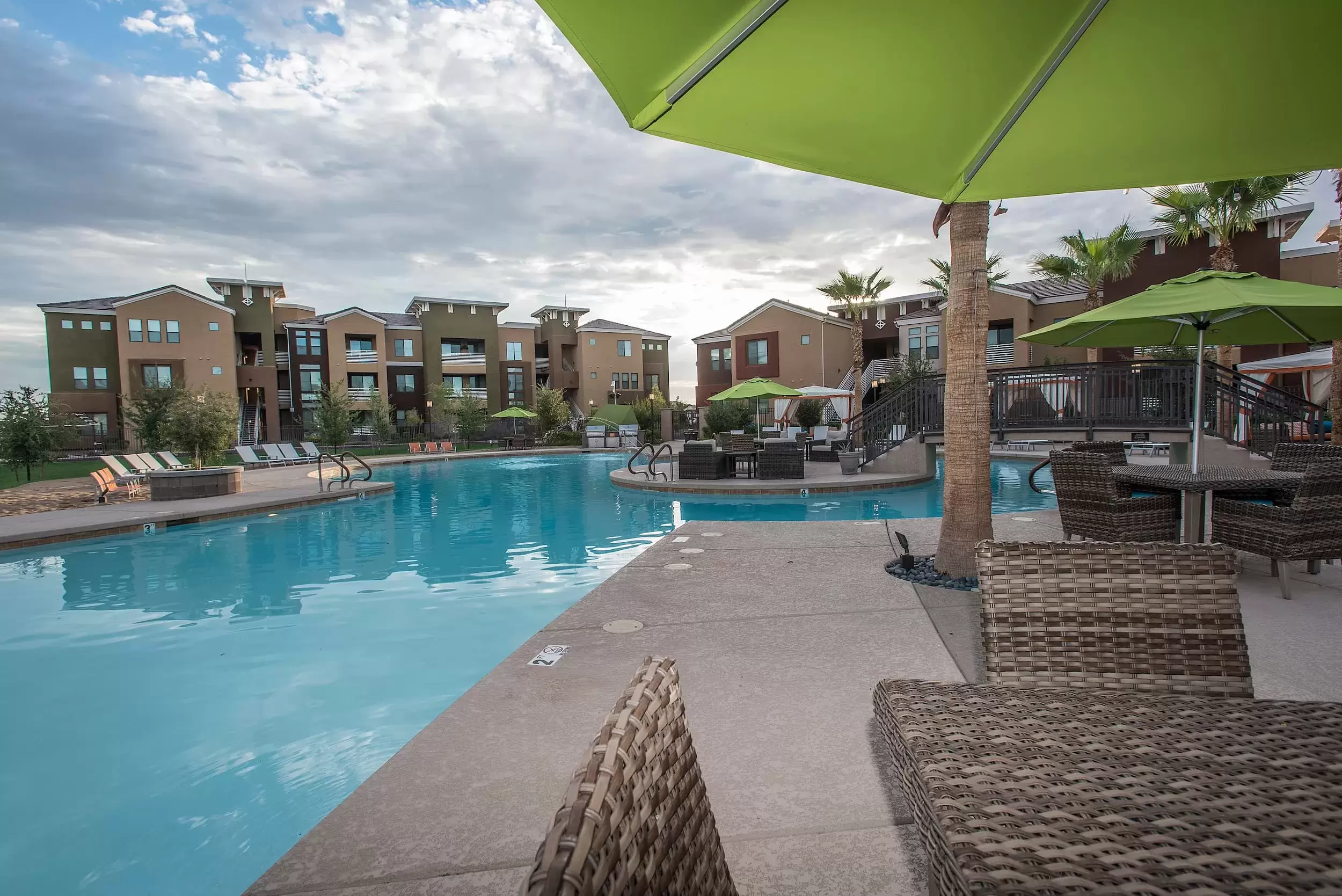 Chairs and tables with umbrellas on the pool deck at the luxury apartment complex.